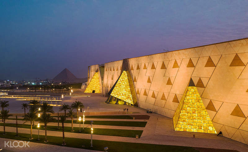 Grand Egyptian Museum exterior with visitors entering the modern glass building near the Giza Plateau.