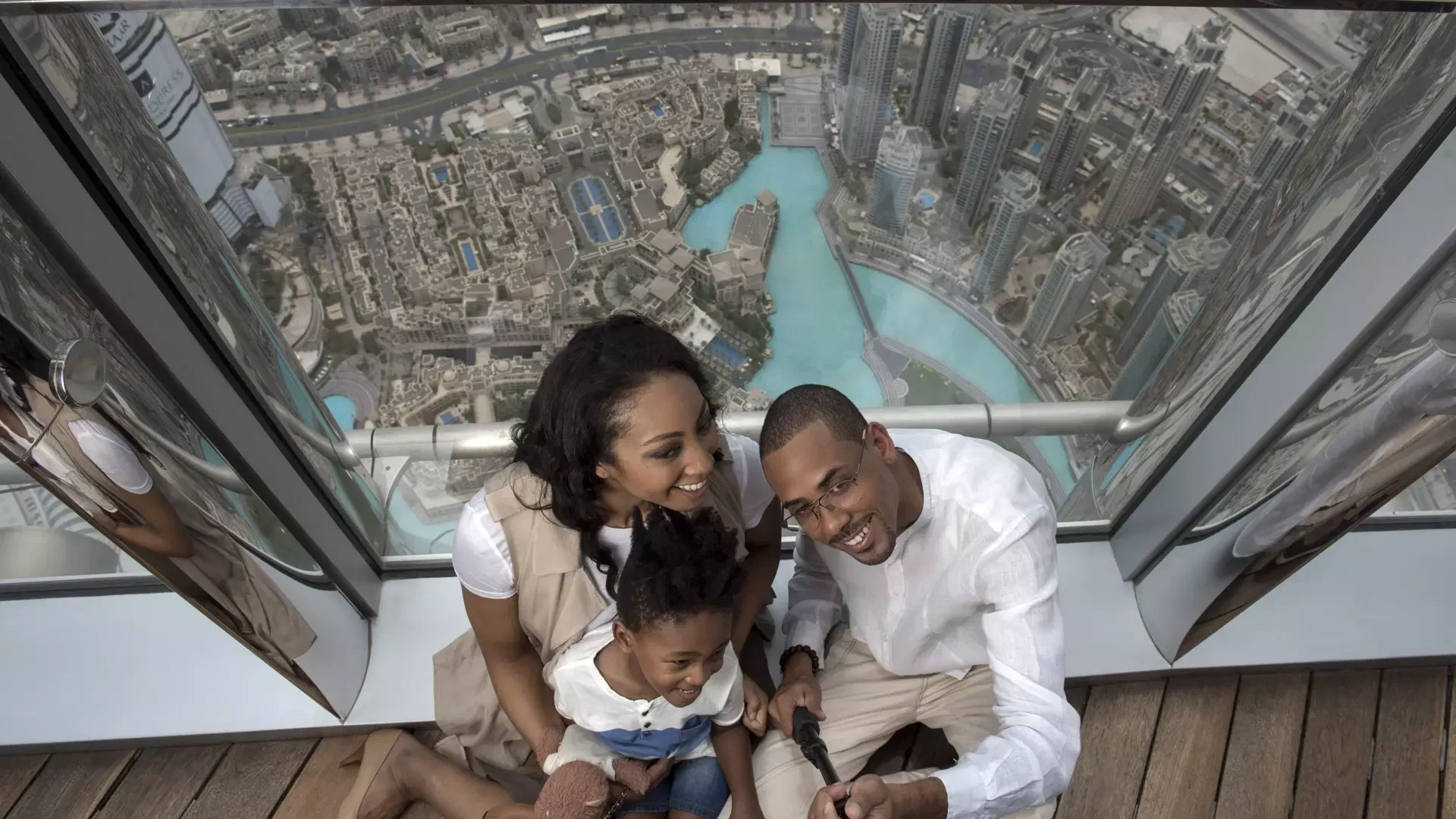 A smiling family taking a selfie on the deck with the fountain lake and Downtown Dubai directly below them at Burj Khalifa