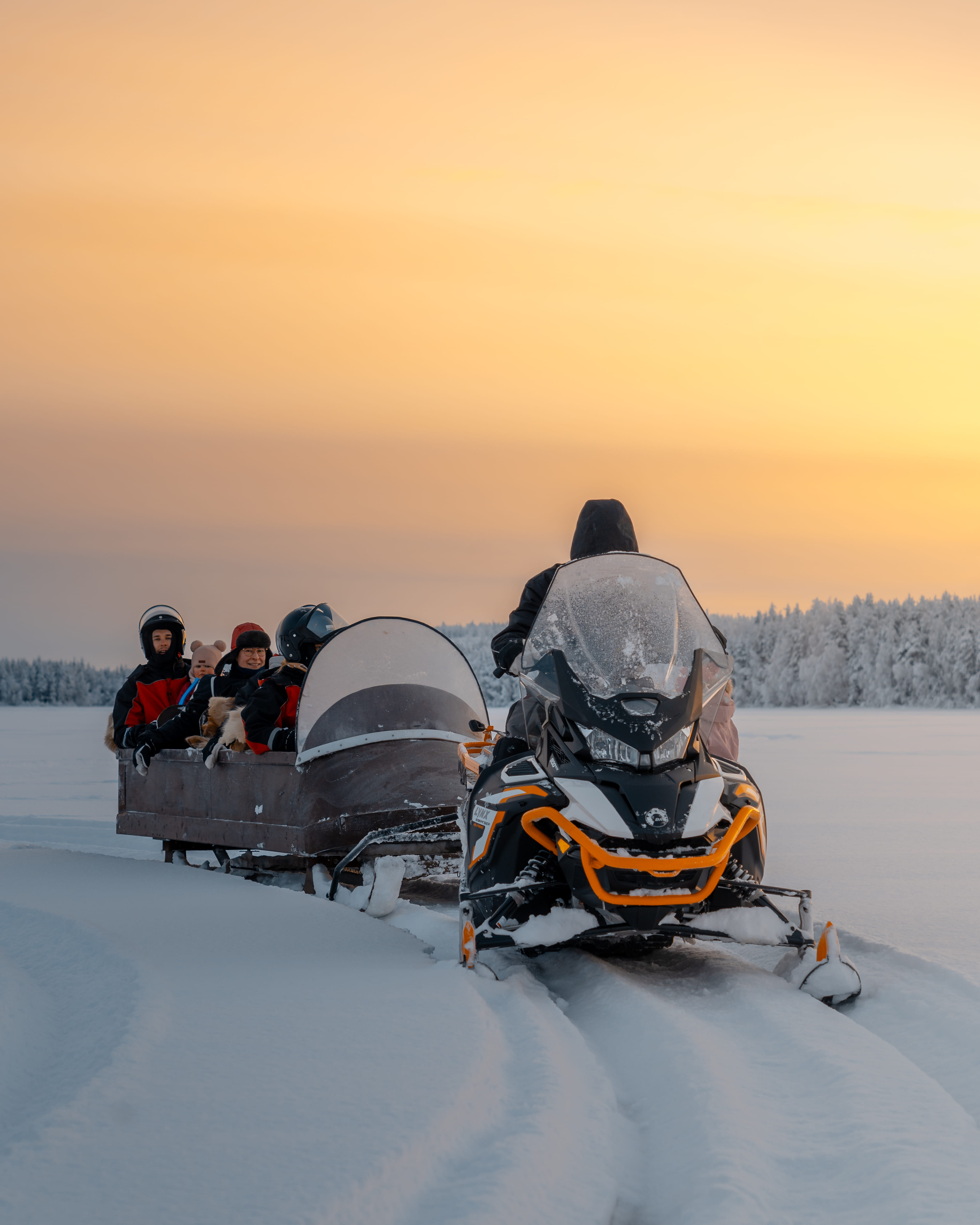 Group riding Snowmobiles across a snowy lake in Rovaniemi with StayLapland.