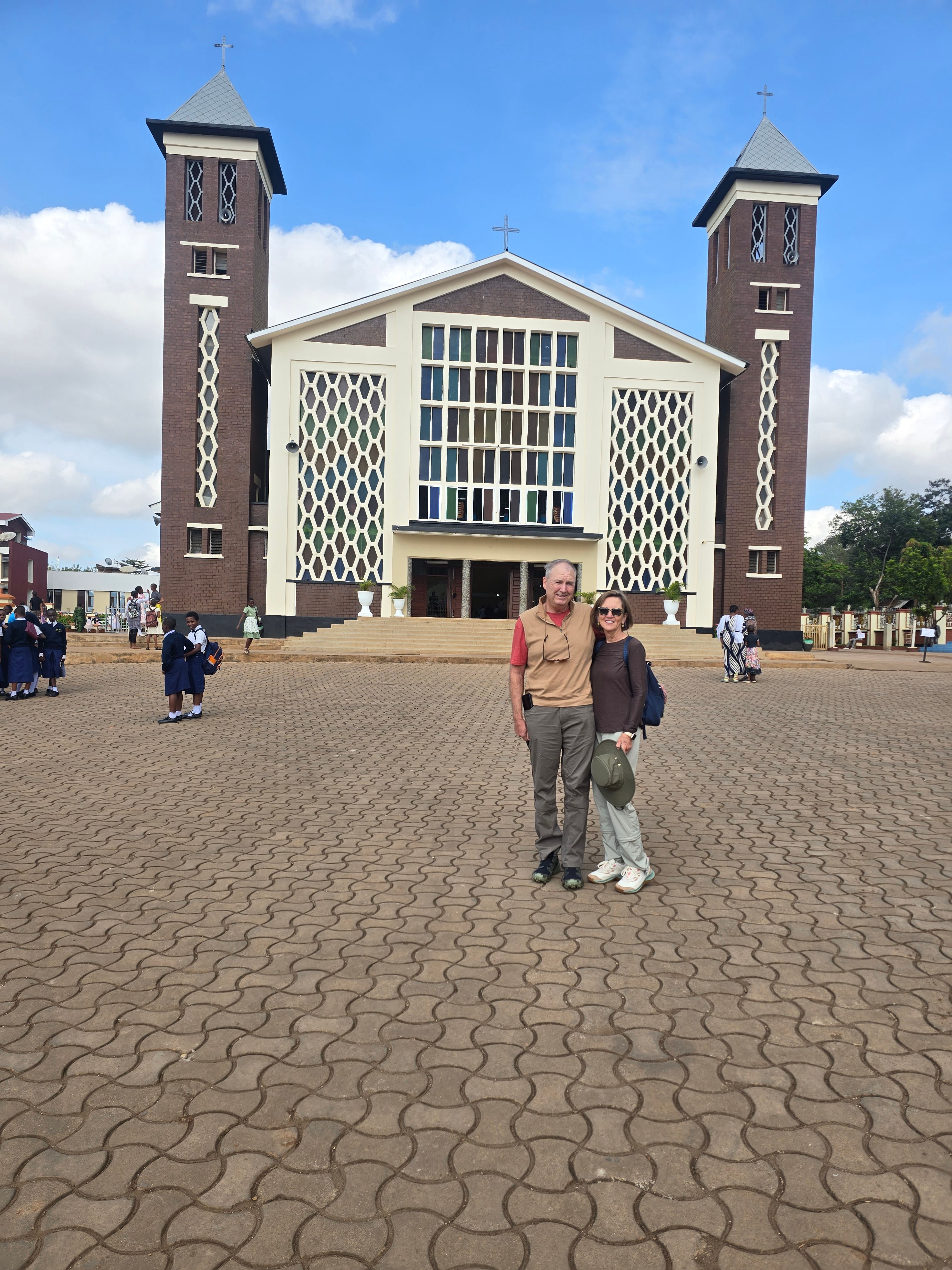 Two visitors posing in the paved courtyard in front of Christ the King Cathedral in Moshi town.