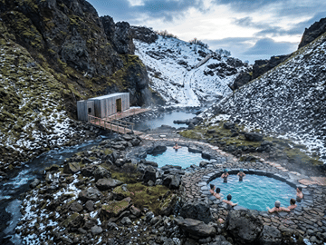 Steam rises from the geothermal pools at Húsafell Canyon Baths as guests soak between snow-dusted lava walls