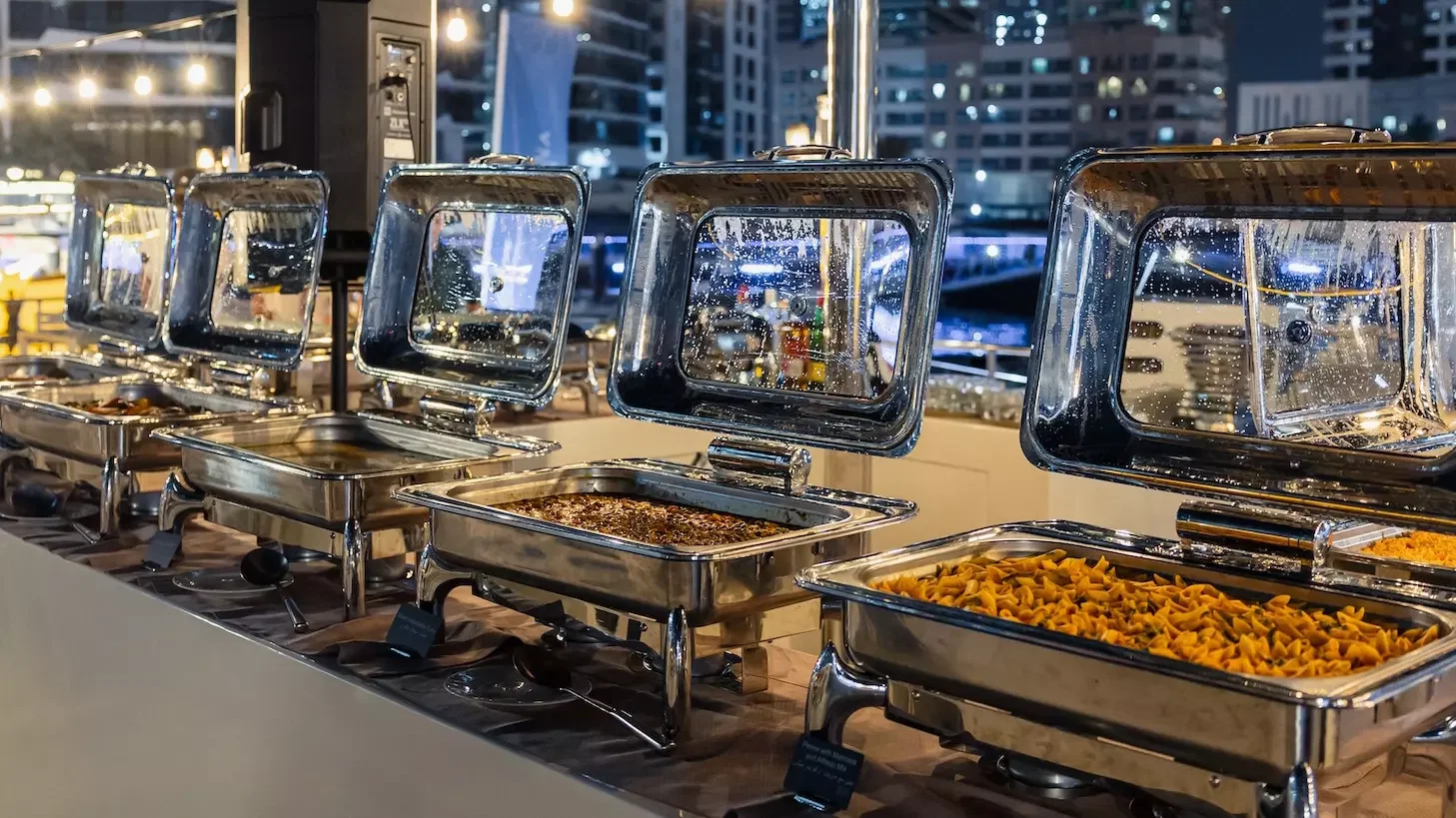 A row of metallic chafing dishes containing various hot foods sits on a buffet table at Alexandra Sea Lounge.
