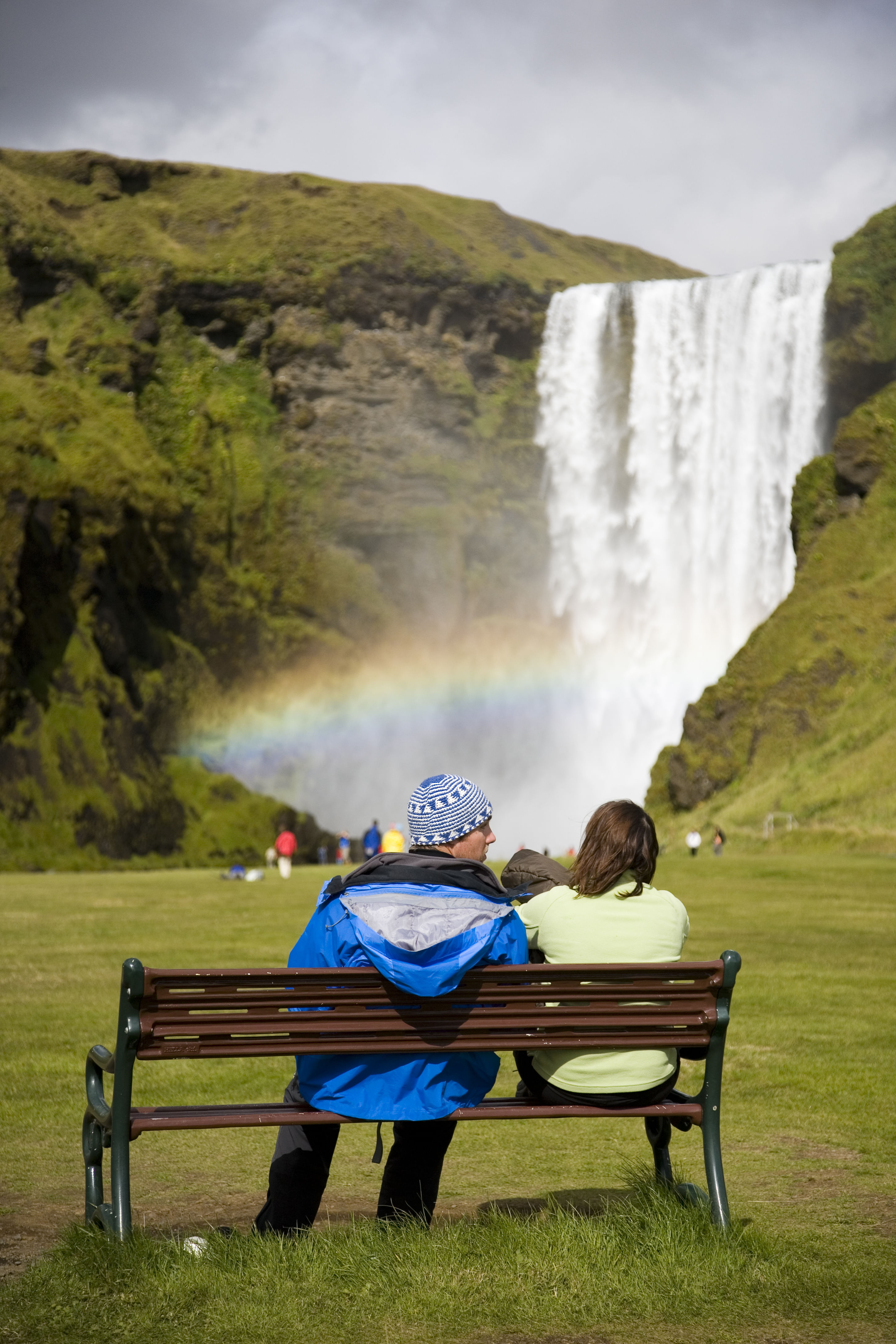 Couple sitting at the bench overlooking Skógafoss Waterfall