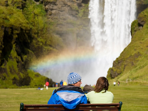 Couple sitting at the bench overlooking Skógafoss Waterfall