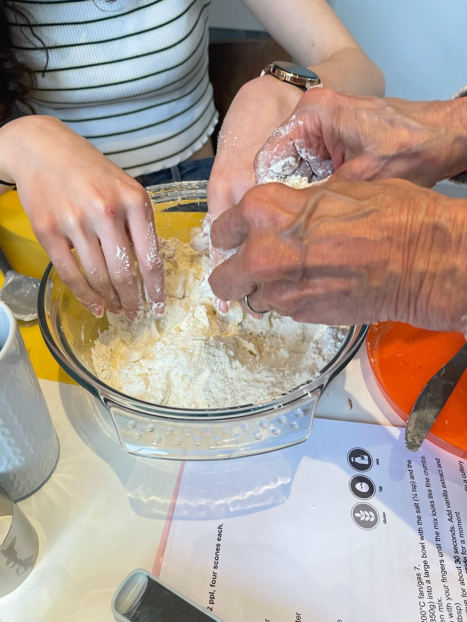 Two sets of hands working together over a bowl making scones