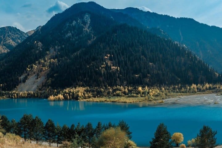 Turquoise alpine lake surrounded by green mountains and blue sky at Issyk Lake, Kazakhstan