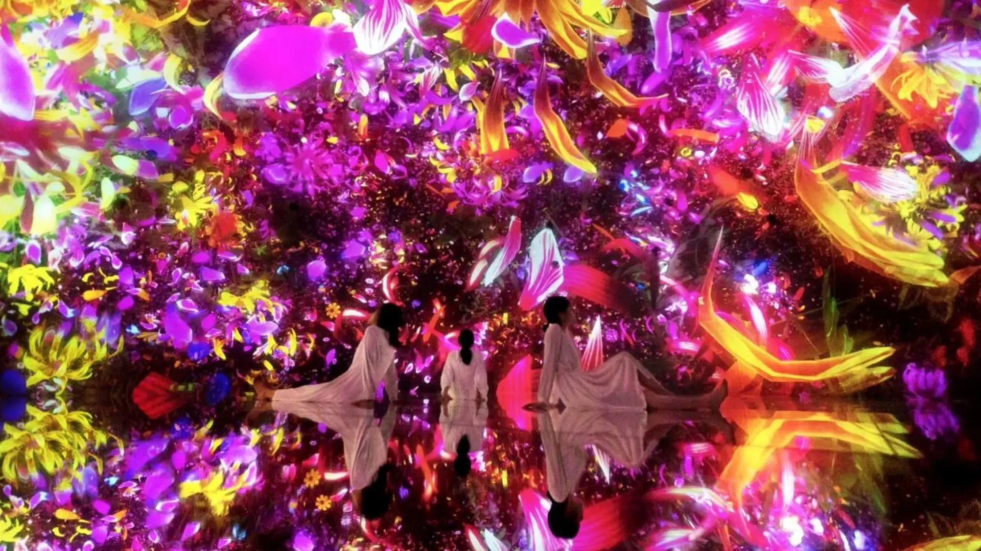 Three people in white dresses sit on a reflective floor beneath a ceiling projection of colorful, falling flower petals at COMBO: Tokyo Skytree + teamLab Planets TOKYO Tickets.