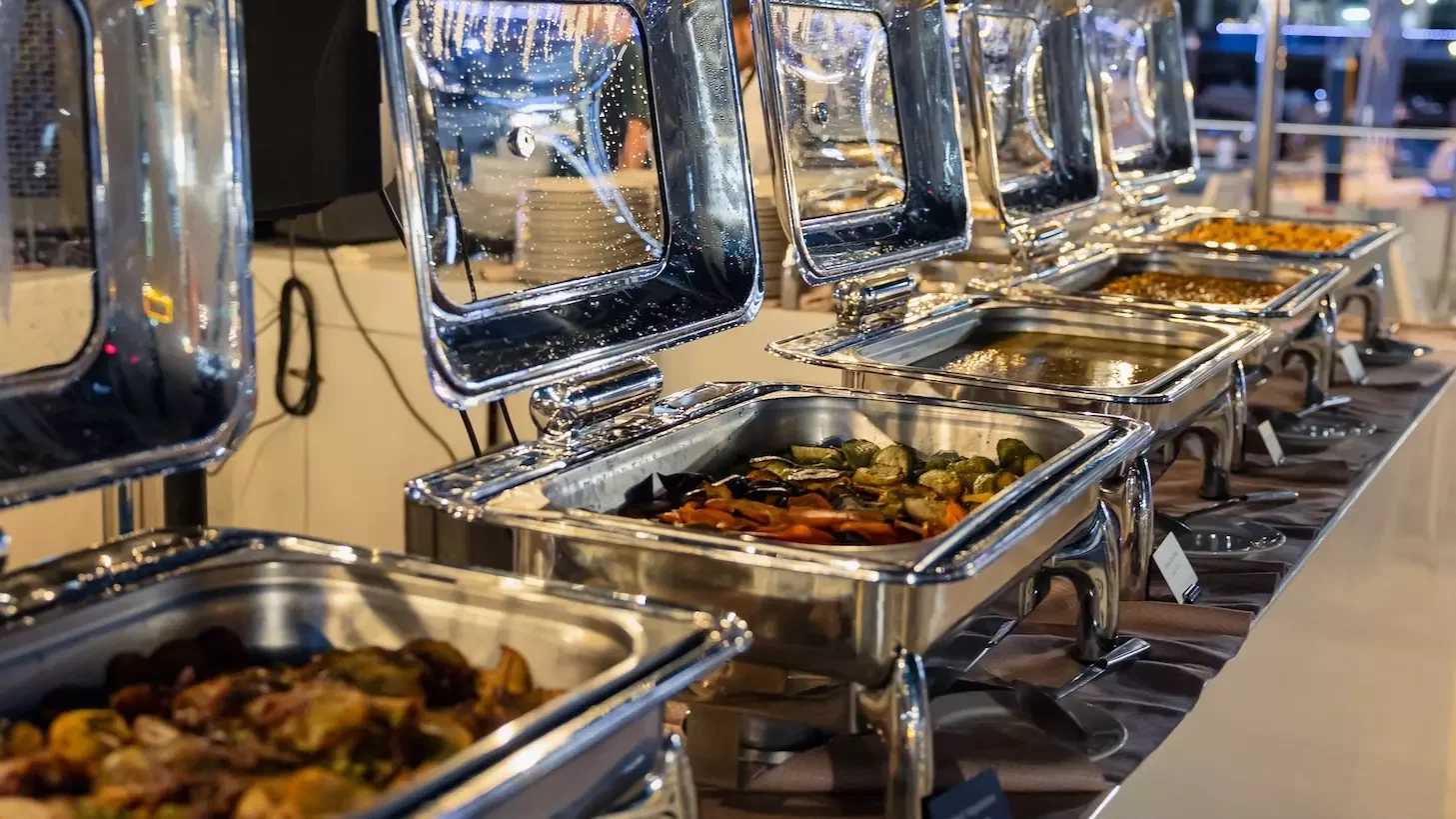 A close-up shot of a buffet line featuring silver chafing dishes filled with roasted vegetables and other dishes at Alexandra Sea Lounge.