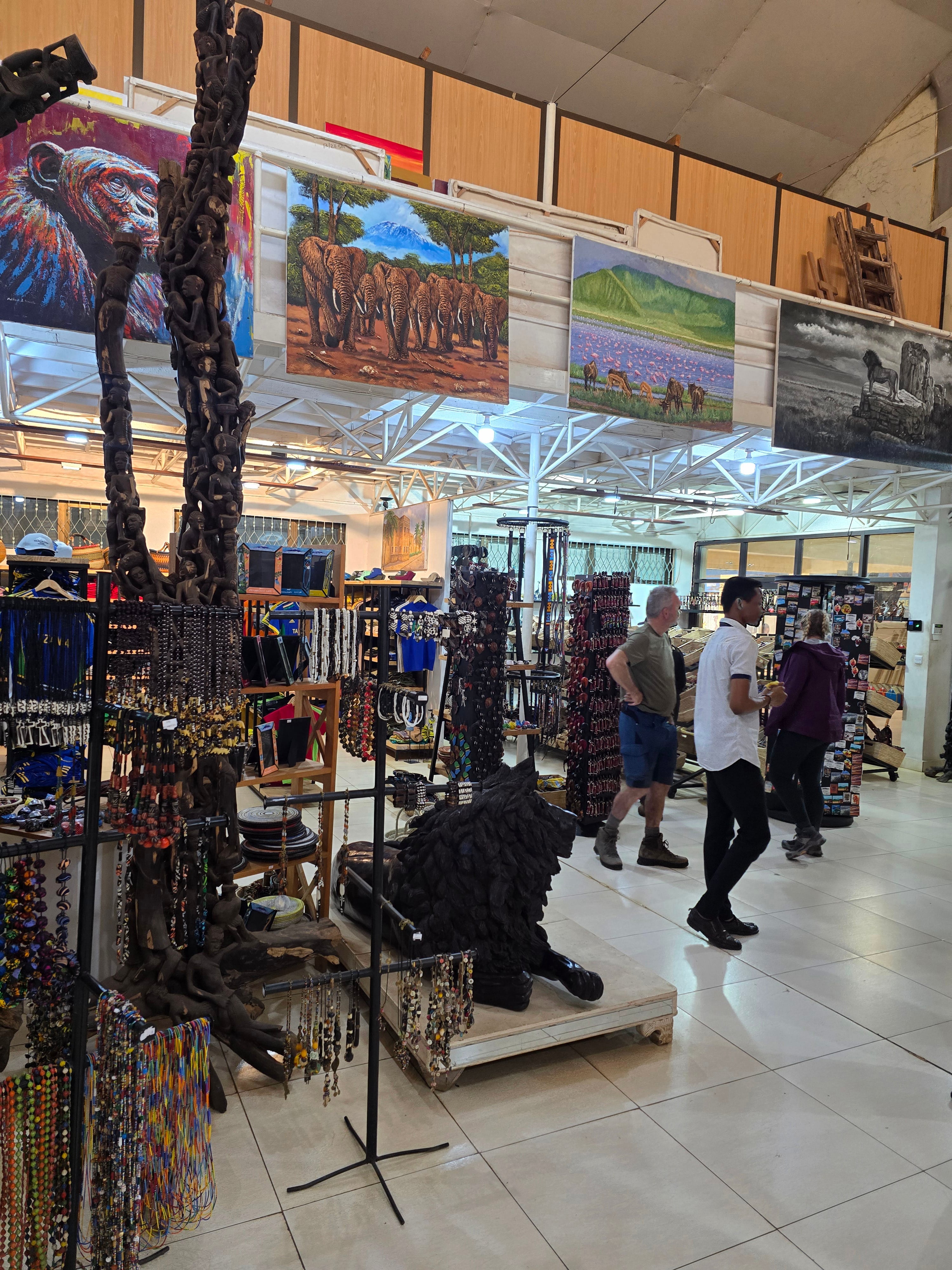 Visitors exploring a brightly lit gift gallery featuring African artwork, carvings, and local souvenirs.