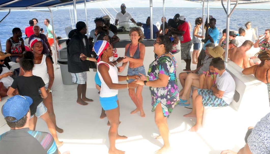 “Varias personas bailando y celebrando en la cubierta de un bote durante una excursión a Isla Saona, acompañadas de música y fiesta