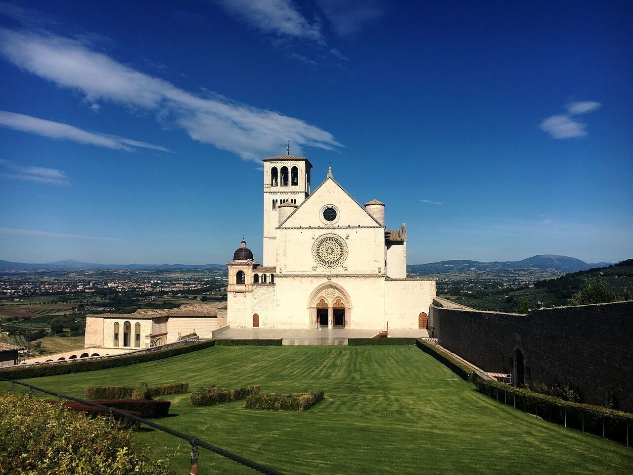 Frontal view of St. Francis Basilica in Assisi with a green meadow in front of it 
