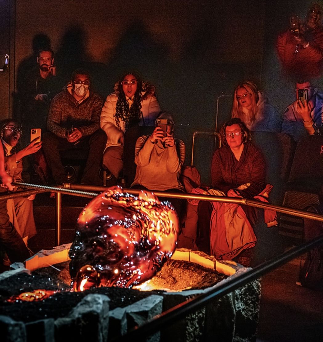 Audience members sit in close proximity watching a large, glowing, freshly-cooled lava formation, with several people photographing the mome