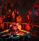 Audience members sit in close proximity watching a large, glowing, freshly-cooled lava formation, with several people photographing the mome