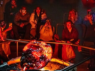 Audience members sit in close proximity watching a large, glowing, freshly-cooled lava formation, with several people photographing the mome