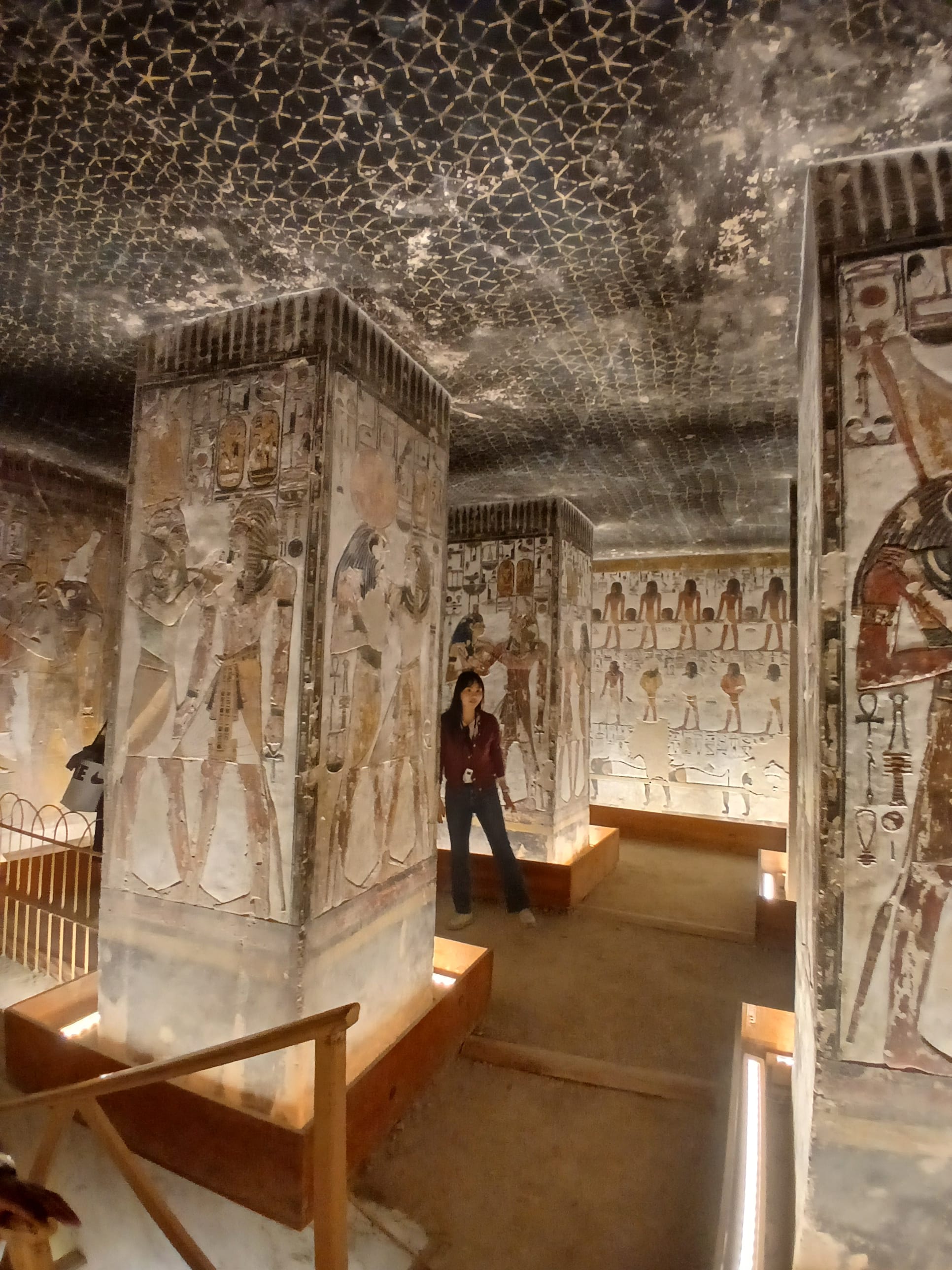 A visitor standing inside a lit chamber with painted stone pillars and colorful ancient hieroglyphic reliefs 