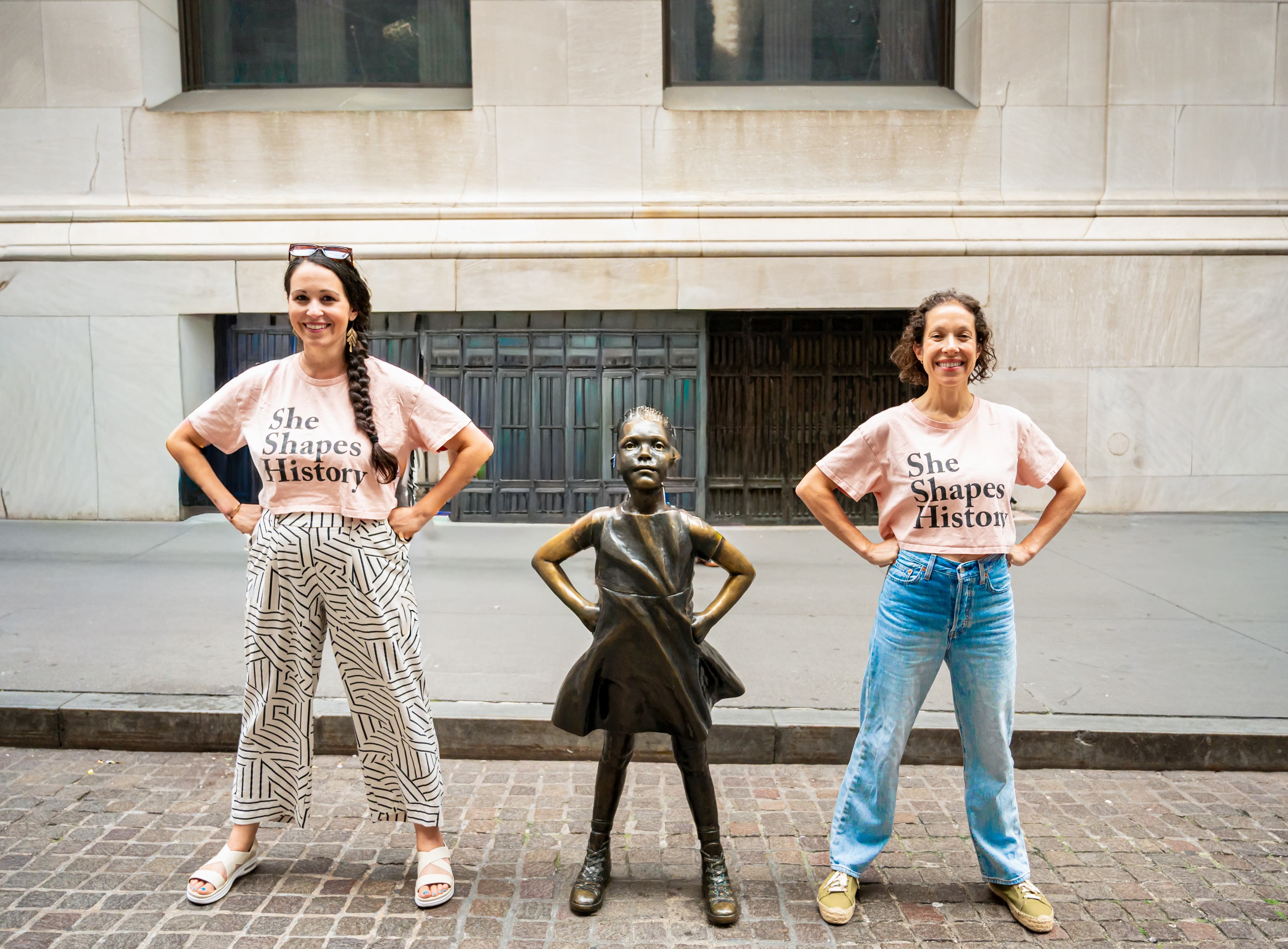 Beth and Nikki, founders of She Shapes History NYC, pose with the iconic Fearless Girl statue on Wall Street.