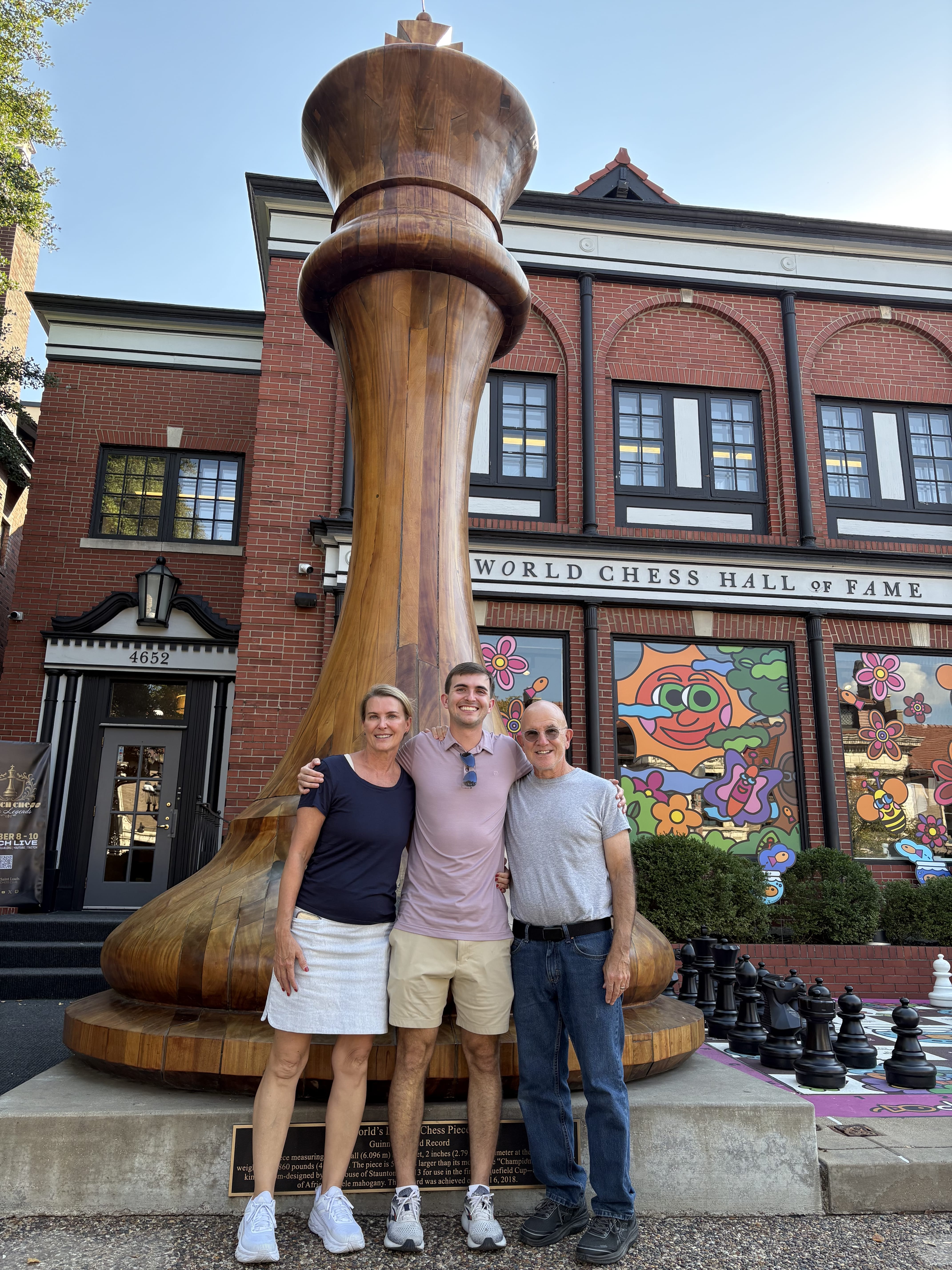 Three tour guests posing in front of the giant wooden king chess piece outside the World Chess Hall of Fame in St. Louis