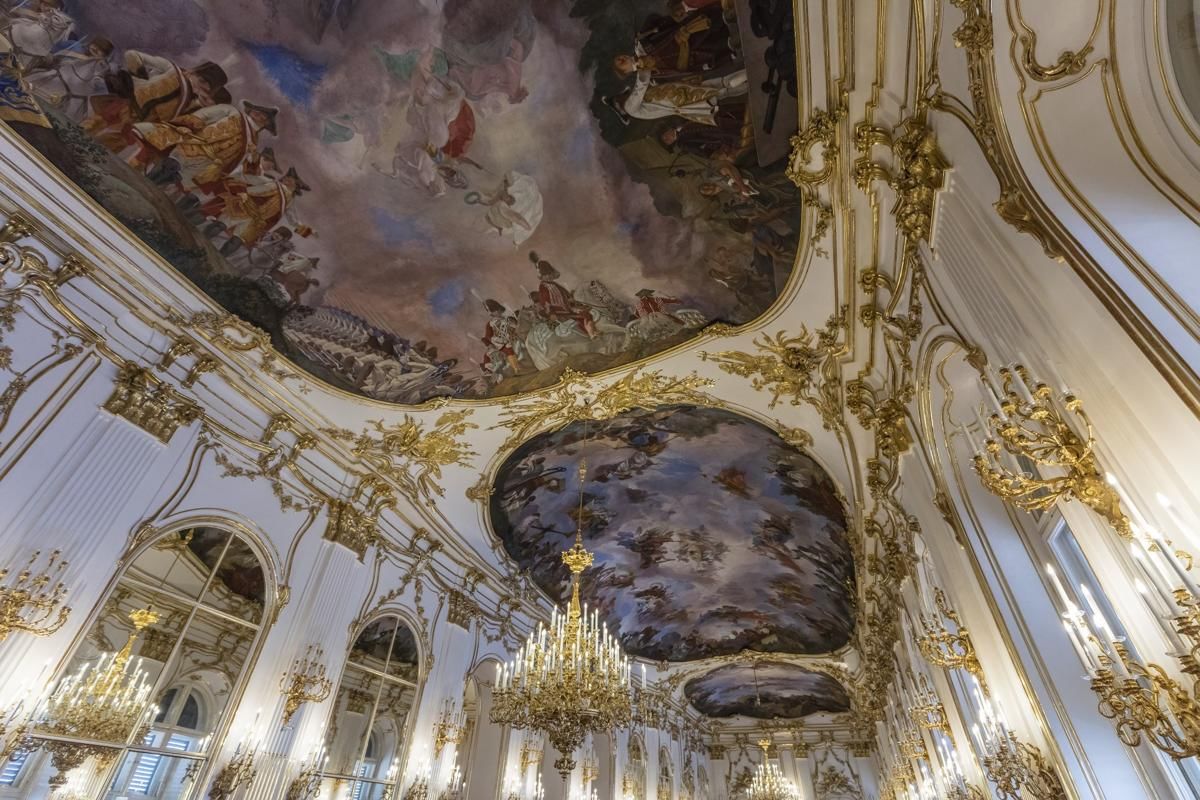 Close-up view of the Great Gallery’s ceiling in Schönbrunn Palace, showing vivid fresco paintings surrounded by elaborate gold trim.
