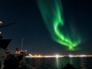 A vivid green Northern Lights display seen from a boat off the coast of Reykjavík.