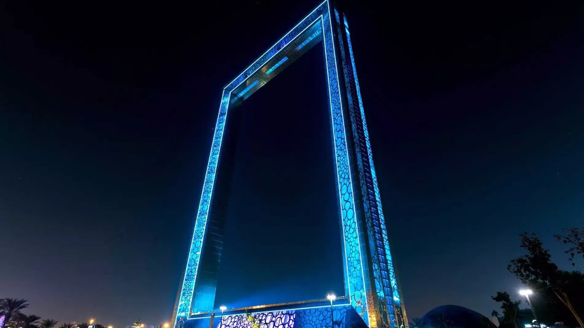The whole frame lit electric blue against a black night sky, its ring-patterned cladding glowing from base to crossbeam at Dubai Frame