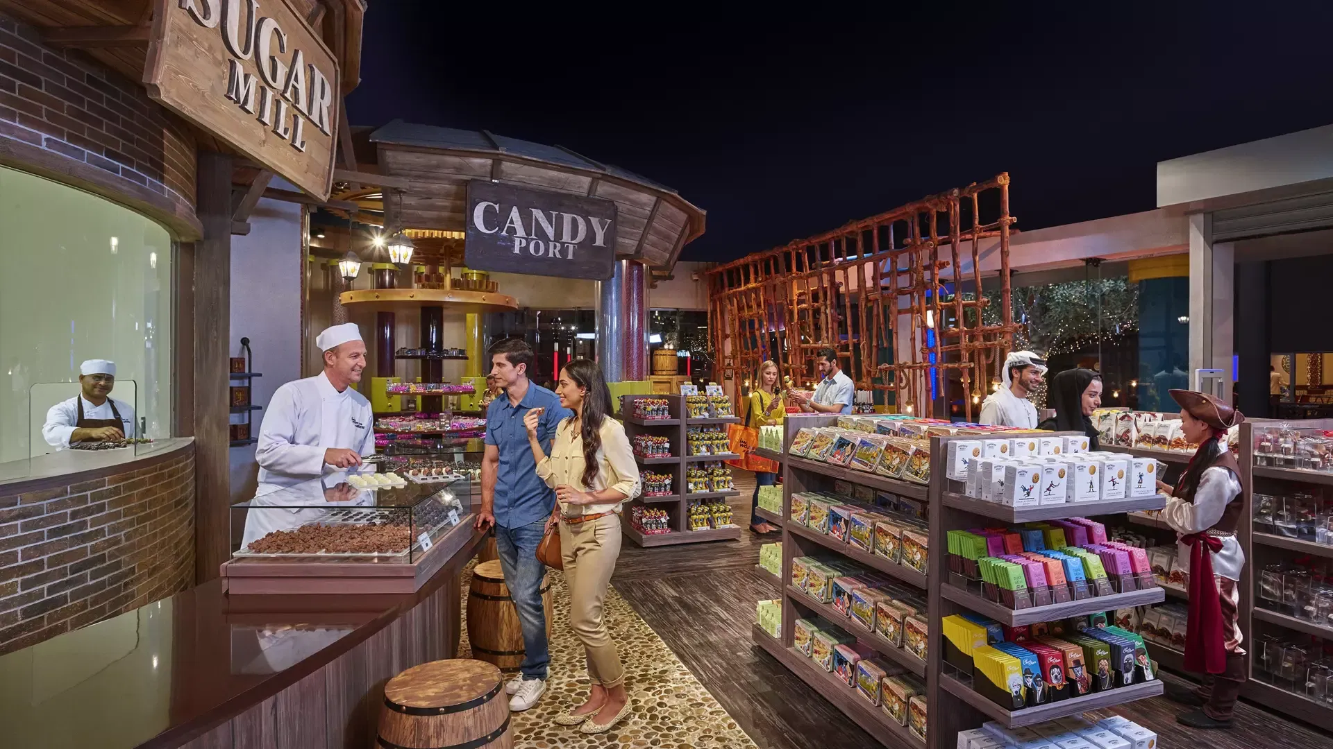 A chef behind a counter talks to a couple inside a candy shop at IMG Worlds of Adventure Theme Park.