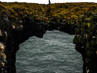 Traveller walking over a rock formation that suspends over the ocean