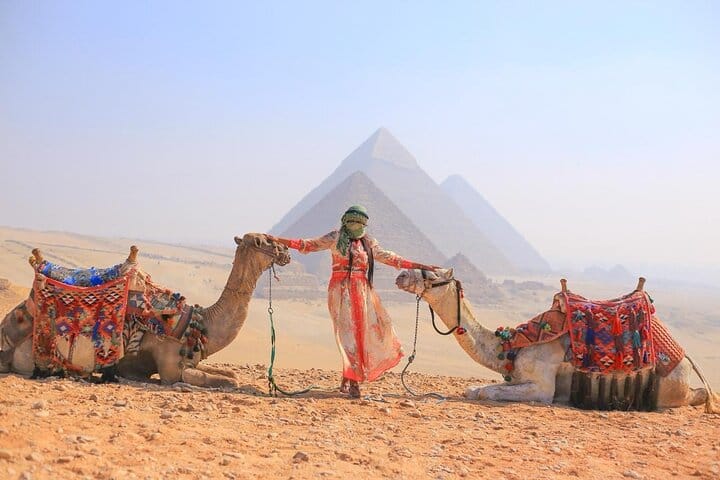 Tourist enjoying a camel ride with the Pyramids and Sphinx in the background during a guided tour in Giza.