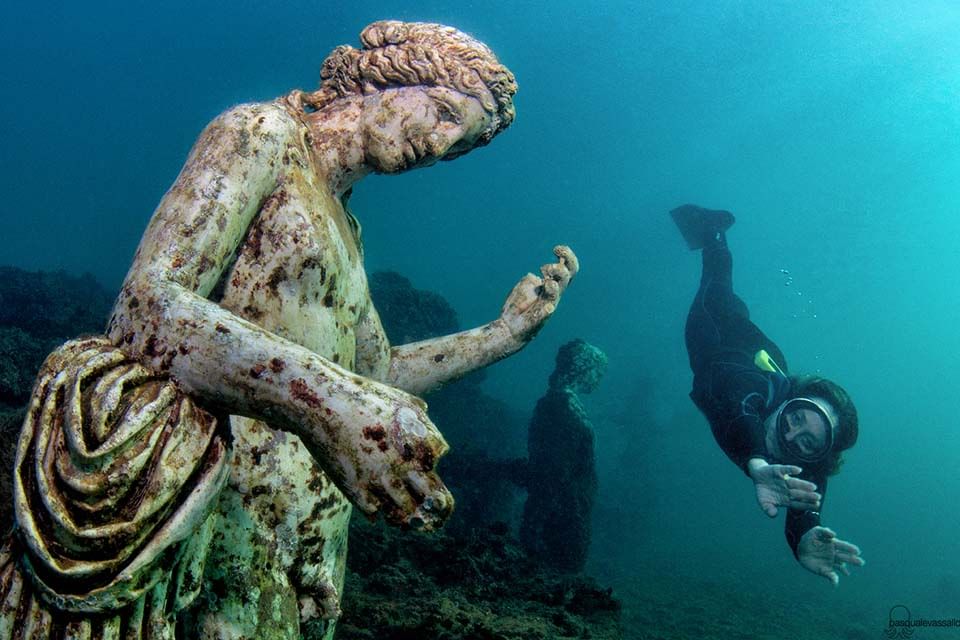 Snorkeler diving to give a closer look at one of the statues of the Ninfeo di Claudio