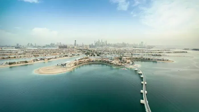 A high-angle vista looks down over coastal waters, landmasses, bridges, and a distant skyline at The Dubai Balloon at Atlantis.