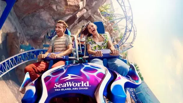 Two guests riding a SeaWorld Abu Dhabi roller coaster car through a rocky themed attraction area at SeaWorld Abu Dhabi.