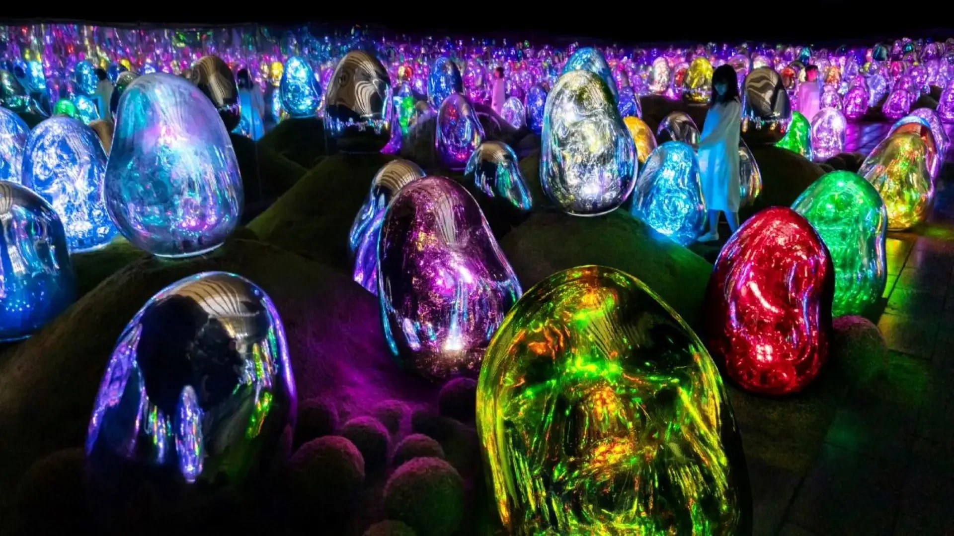 A visitor walks among glowing, colorful, egg-shaped sculptures arranged on a dark landscape at COMBO: Tokyo Skytree + teamLab Planets TOKYO Tickets.