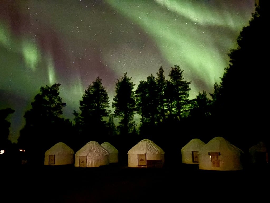 Northern Lights glowing above traditional yurts in the dark Arctic wilderness near Levi.