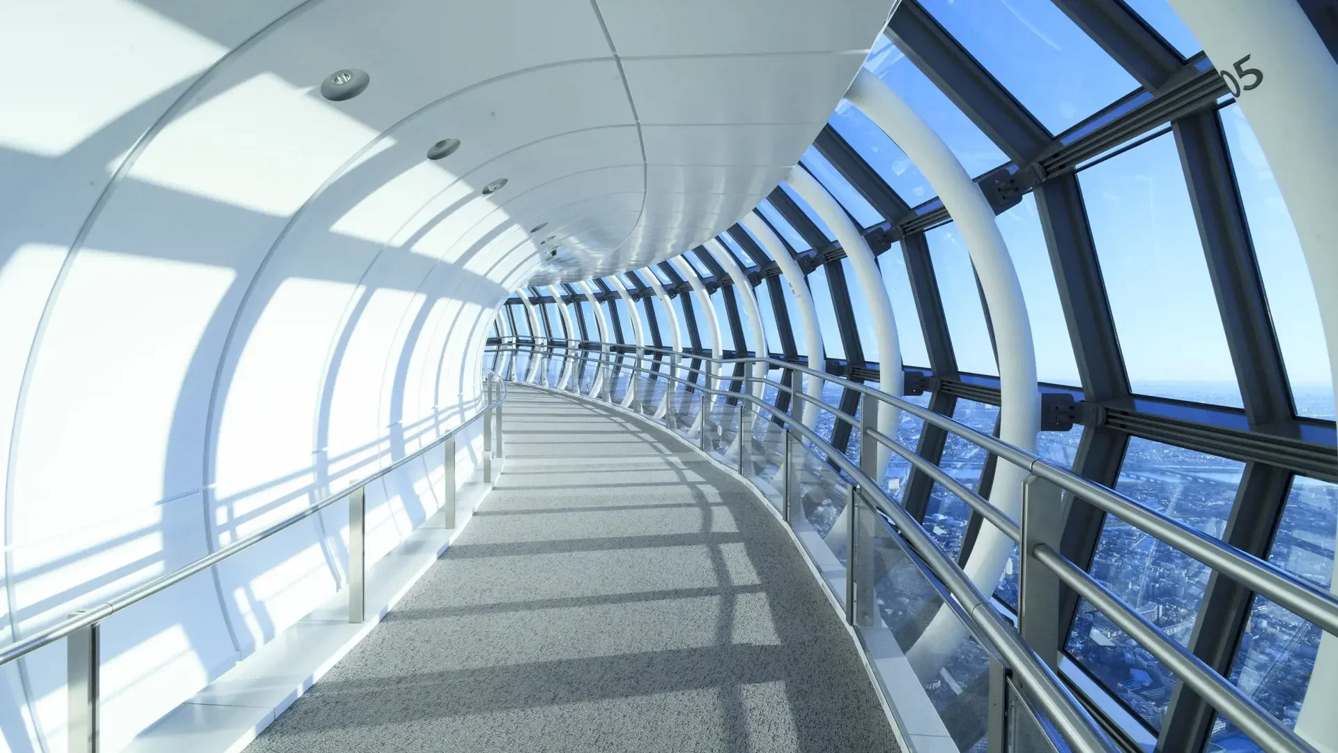 A long, curving hallway with white walls and a carpeted floor is lined with glass windows overlooking a city at COMBO: Tokyo Skytree + teamLab Planets TOKYO Tickets.