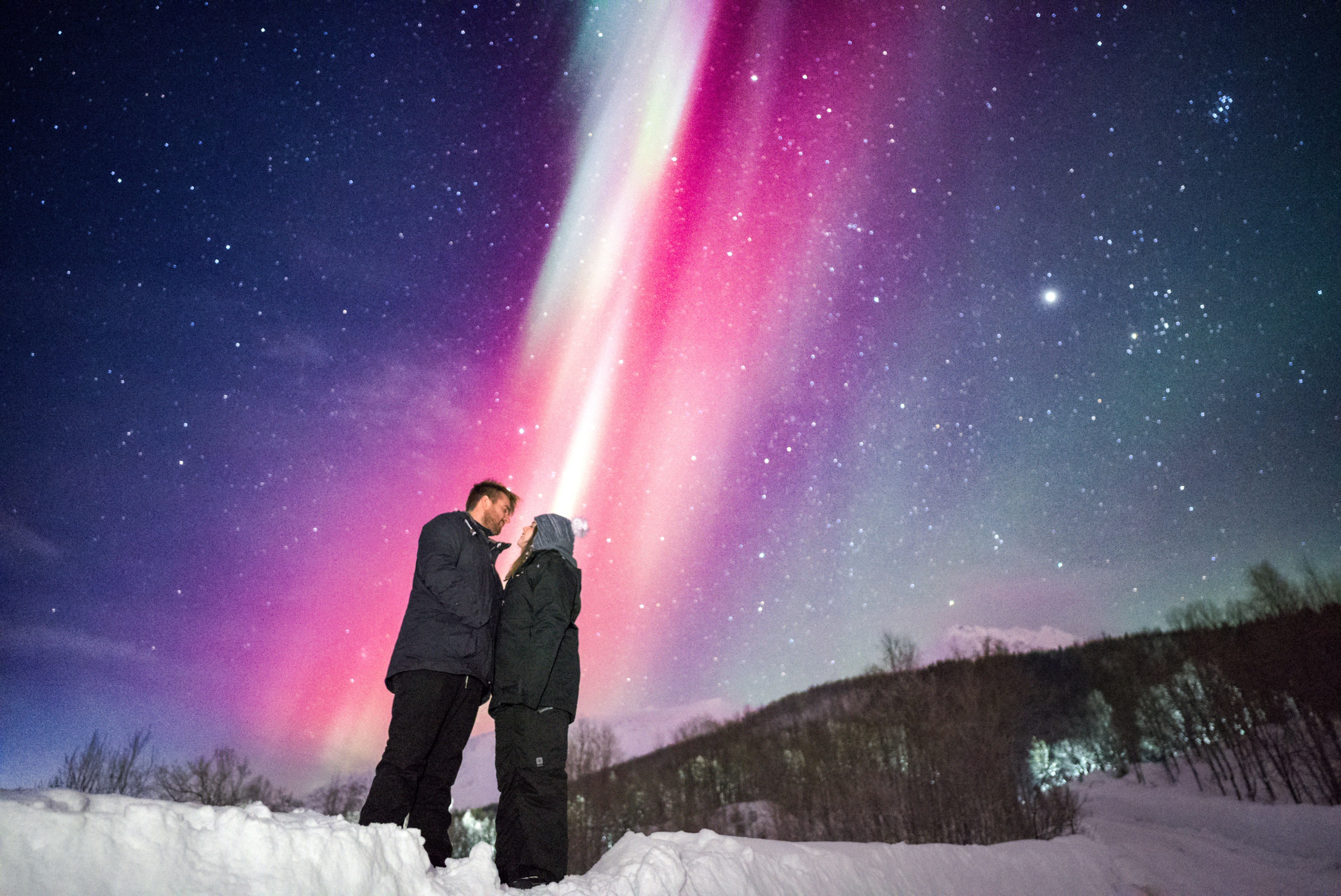 Couple standing together under vibrant pink and green Northern Lights during a private Tromsø Aurora tour.