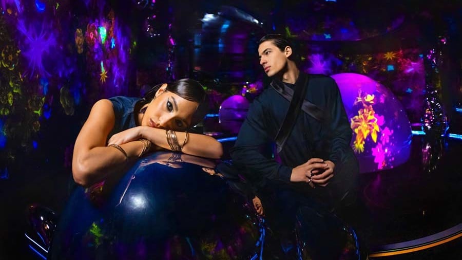 Two visitors beside a large glossy dark-blue sphere at AYA Universe Dubai, with violet and pink floral light projections filling the walls behind them