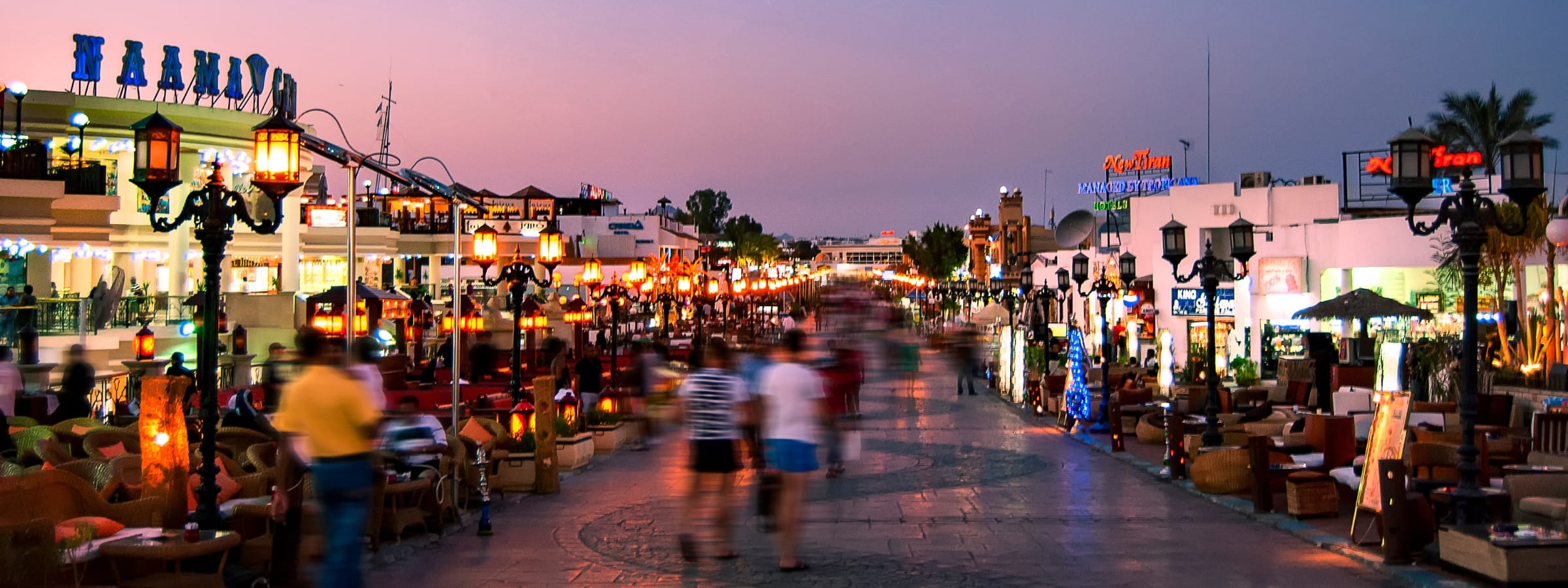 Vibrant nightlife scene on the illuminated Naama Bay walking street in Sharm El Sheikh, Egypt, with blurred people.