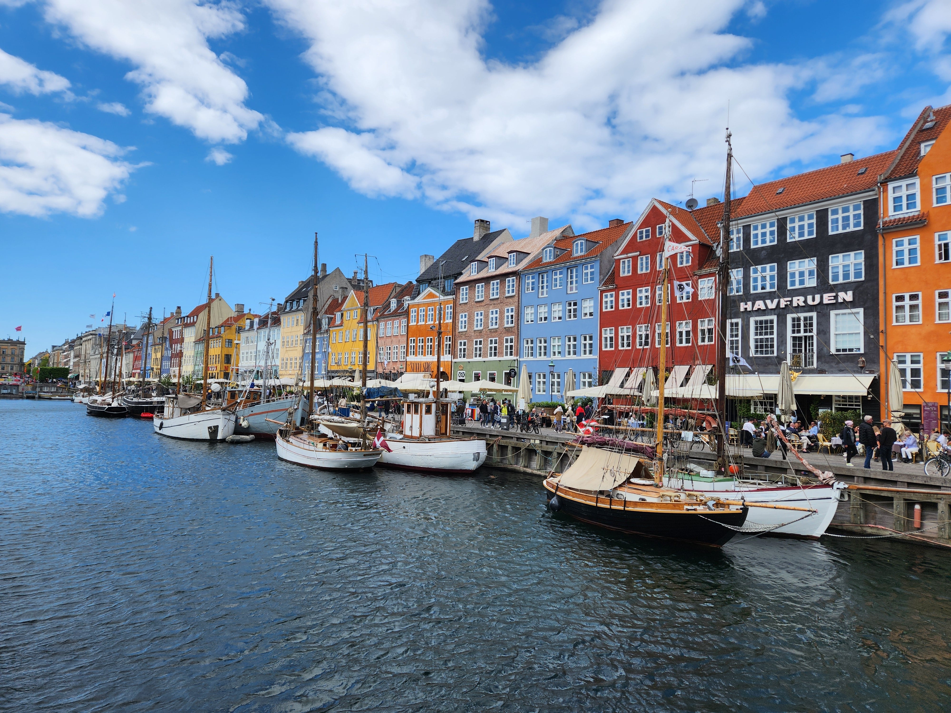 A view of Nyhavn with the colorfull houses and huse boats, and a look into the lively restaurants from the water front