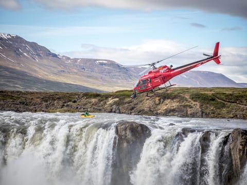 Helicopter flying above a waterfall and Icelandic mountains, highlighting the incredible scenery featured in FlyOver Iceland and sightseeing