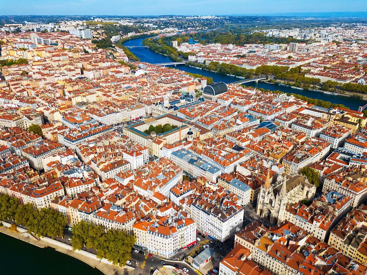Aerial view of Lyon’s Presqu'île, showcasing the red-roofed buildings, the Saône River, and the vibrant cityscape surrounded by green spaces