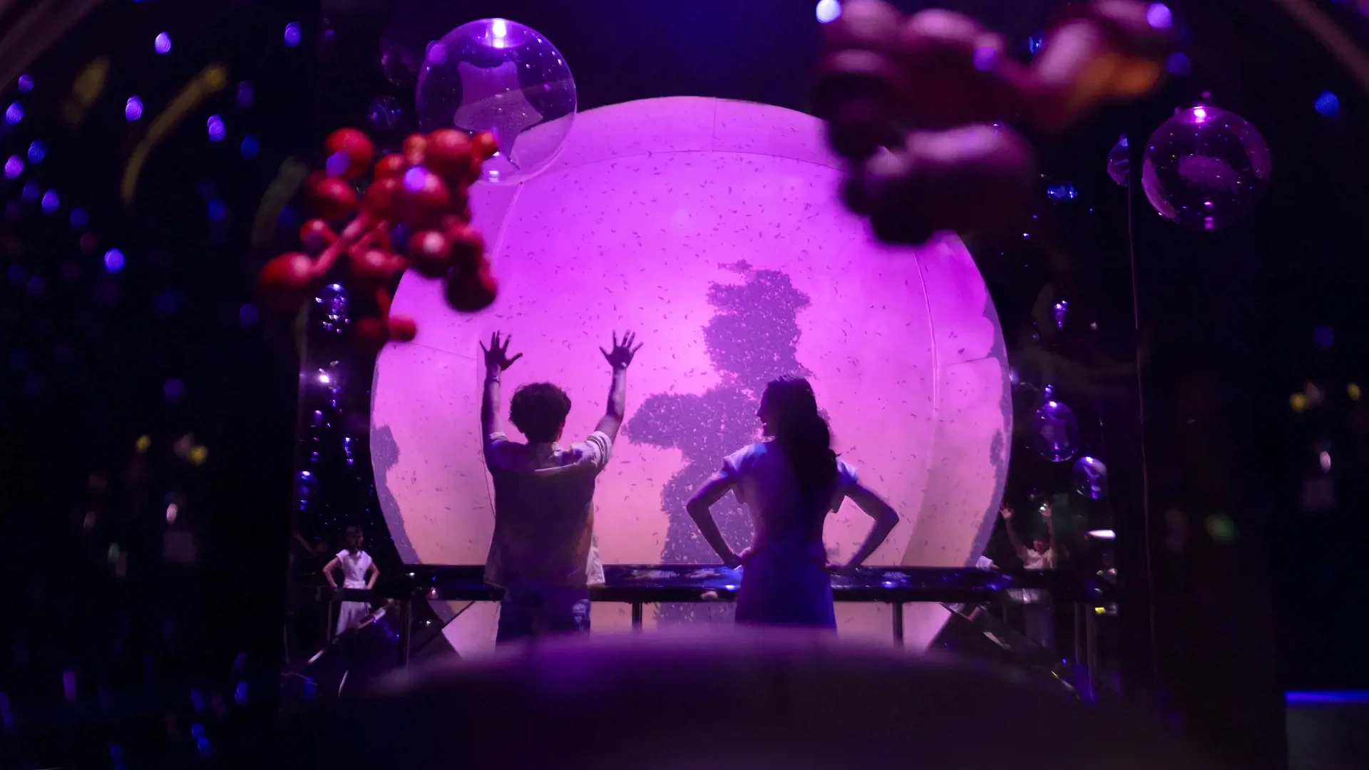 Two people stand before a large, glowing purple sphere projecting silhouetted trees at Exploria in Mandai Singapore Ticket.