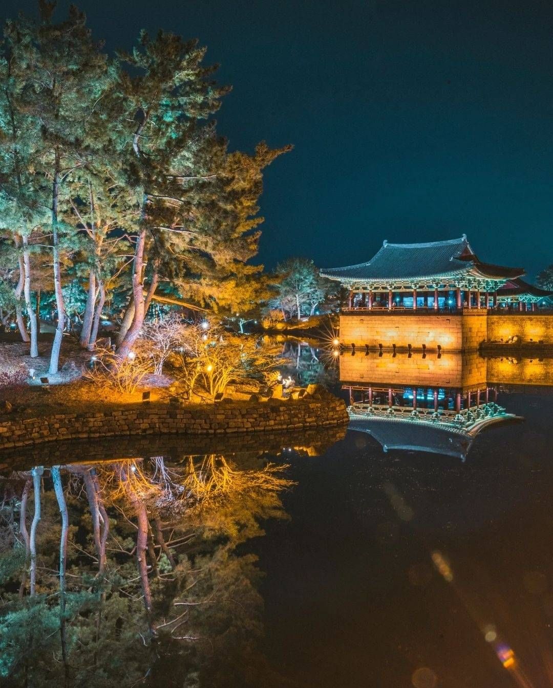 Illuminated pavilion reflected in the water at Wolji Pond during nighttime.