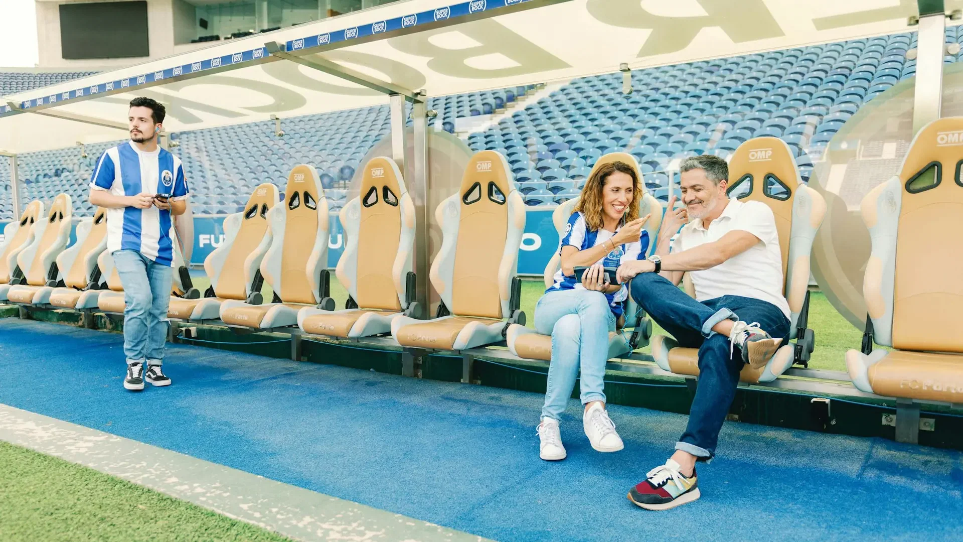 Three people relax on stadium benches beside the pitch while another stands nearby at FC Porto Museum & Dragão Stadium ticket.