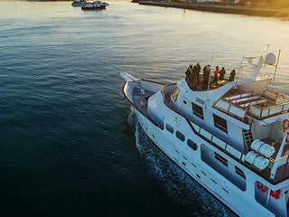 An aerial shot of a yacht with people onboard the deck