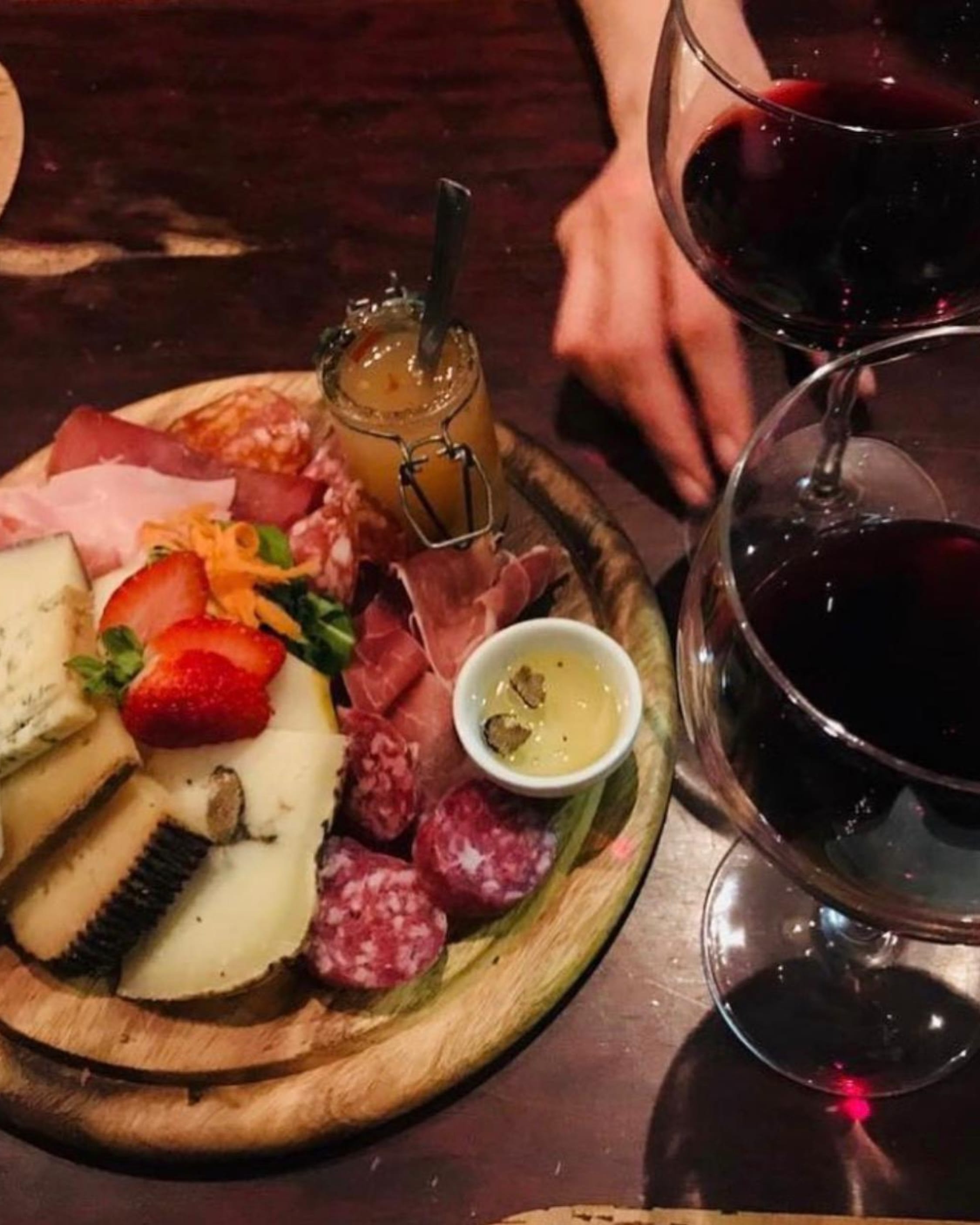 A rich plate of cheeses and cured meats, with deep red wine — a slow, flavorful pause in a Roman wine bar.