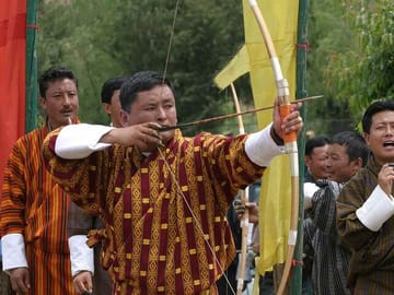 An archer dressed in traditional costumes taking aim at the target