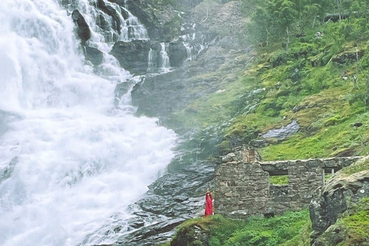 Powerful Kjosfossen waterfall beside a performer dressed in red