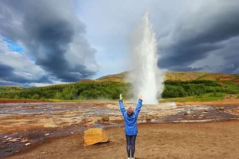 Geysir erupting with happy woman in front