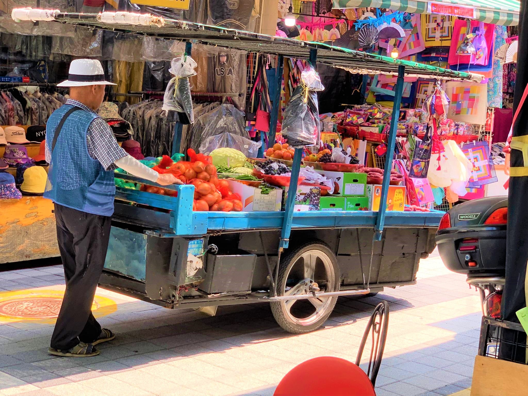 A vendor pushes a cart piled with fresh tomatoes and produce through Gukje Market, a lively traditional market in Busan.