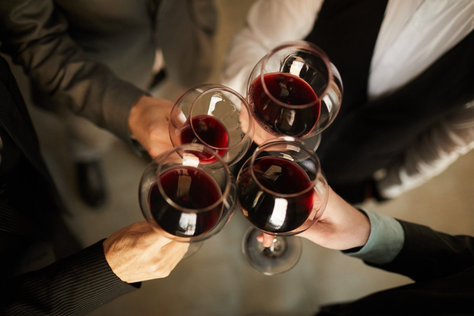 A group of people clinking glasses filled with red wine, celebrating a wine tasting experience in a warm and elegant atmosphere.