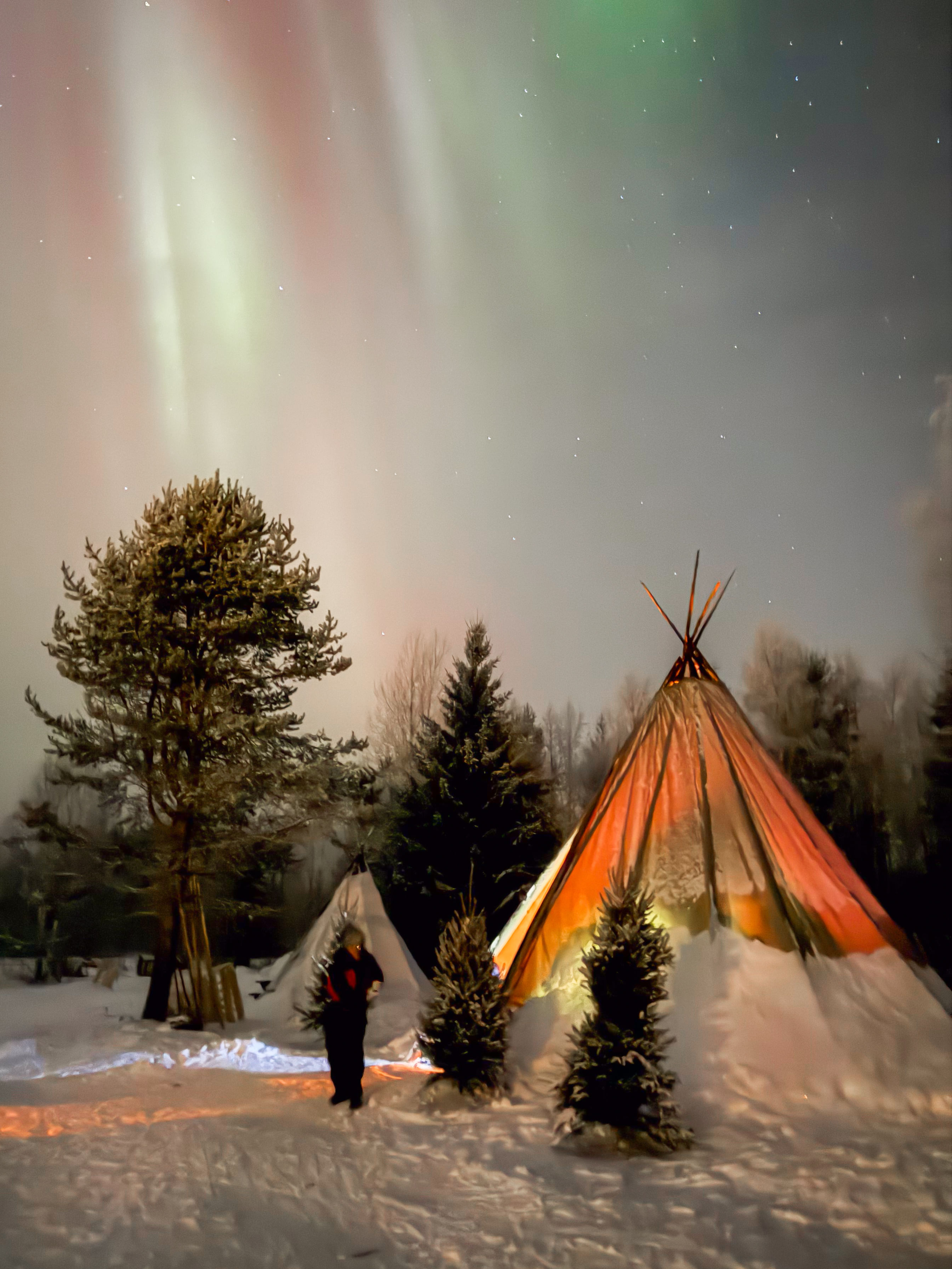 Guests by the fire enjoying the Northern Lights during StayLapland’s Northern Lights Tour Snowmobile Driving in Rovaniemi.